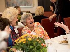 An older woman laughing with others. Links to What to Give